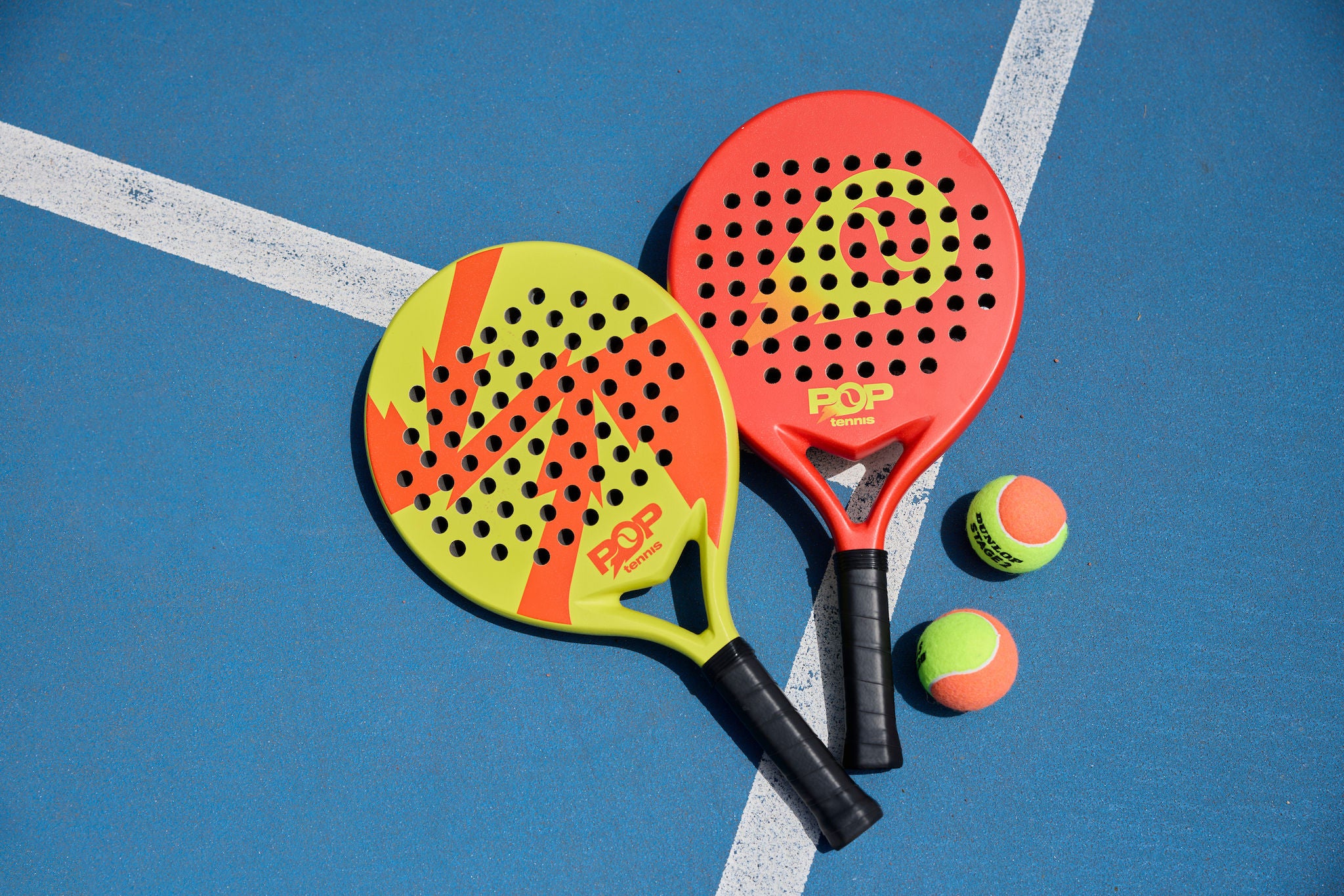 Pop tennis racquets and balls arranged on a on court